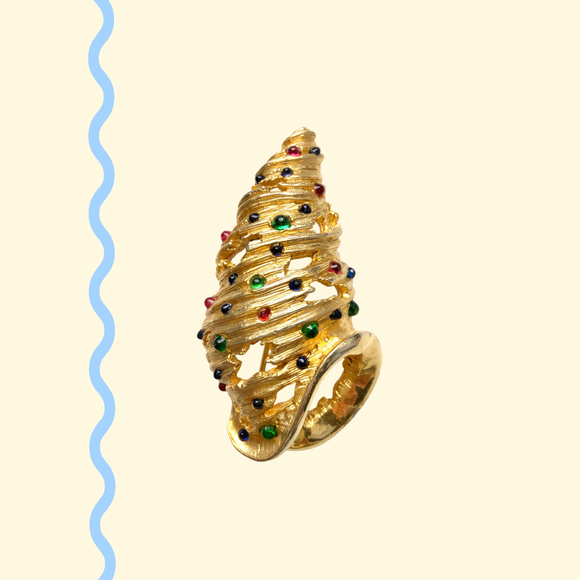 A vintage Alice Caviness brooch featuring a gold-tone spiral shell adorned with colourful glass cabochons. ゴールドトーンの巻貝に、カラフルなグラスカボションがあしらわれた、Alice Caviness のヴィンテージブローチ。