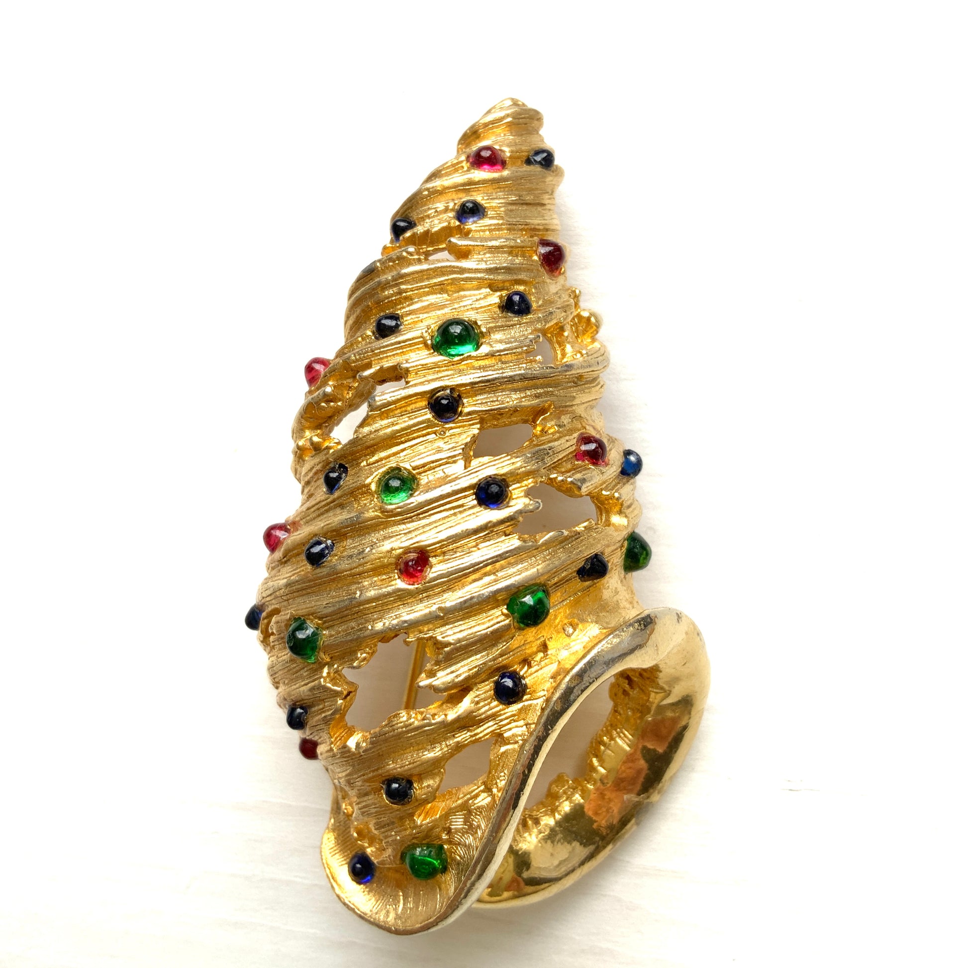 A vintage Alice Caviness brooch featuring a gold-tone spiral shell adorned with colourful glass cabochons. ゴールドトーンの巻貝に、カラフルなグラスカボションがあしらわれた、Alice Caviness のヴィンテージブローチ。