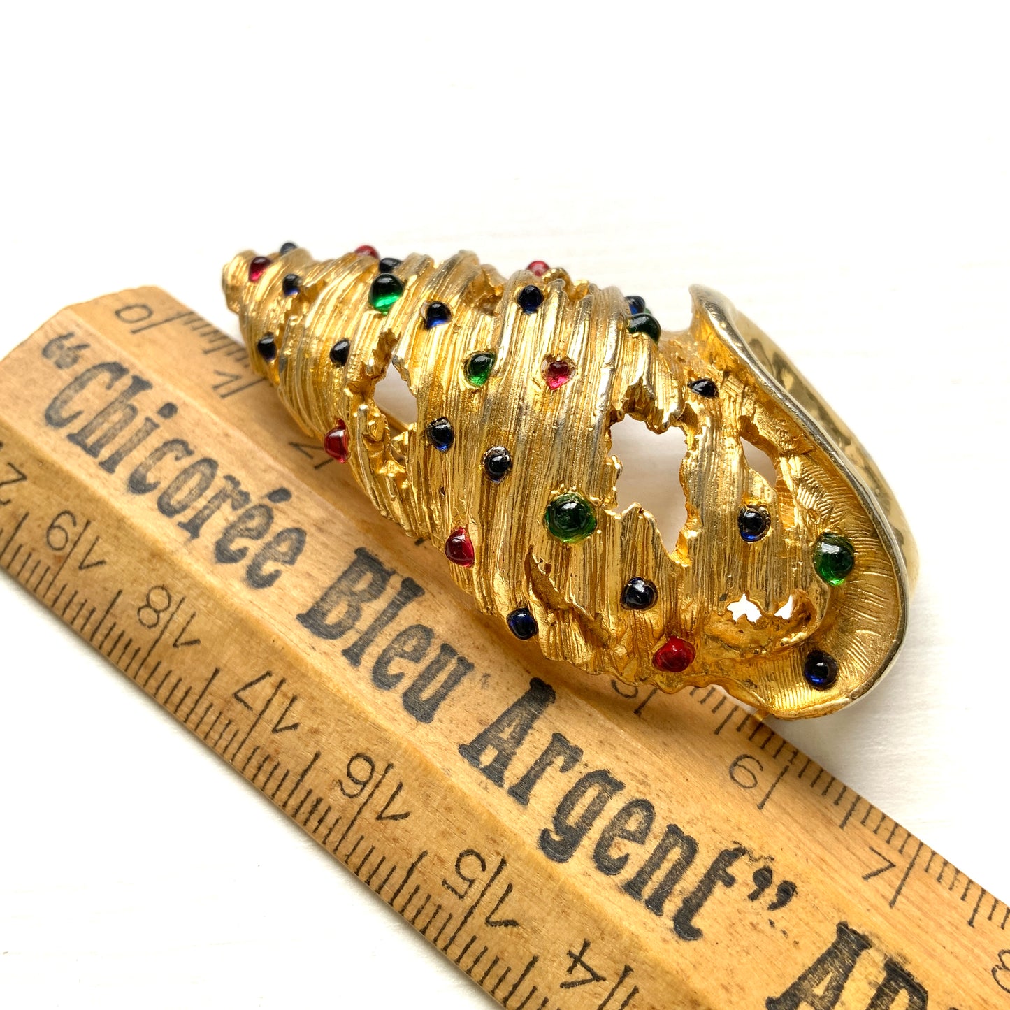 A vintage Alice Caviness brooch featuring a gold-tone spiral shell adorned with colourful glass cabochons. ゴールドトーンの巻貝に、カラフルなグラスカボションがあしらわれた、Alice Caviness のヴィンテージブローチ。
