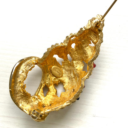 A vintage Alice Caviness brooch featuring a gold-tone spiral shell adorned with colourful glass cabochons. ゴールドトーンの巻貝に、カラフルなグラスカボションがあしらわれた、Alice Caviness のヴィンテージブローチ。