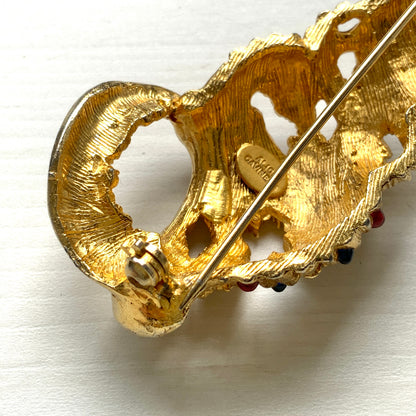 A vintage Alice Caviness brooch featuring a gold-tone spiral shell adorned with colourful glass cabochons. ゴールドトーンの巻貝に、カラフルなグラスカボションがあしらわれた、Alice Caviness のヴィンテージブローチ。