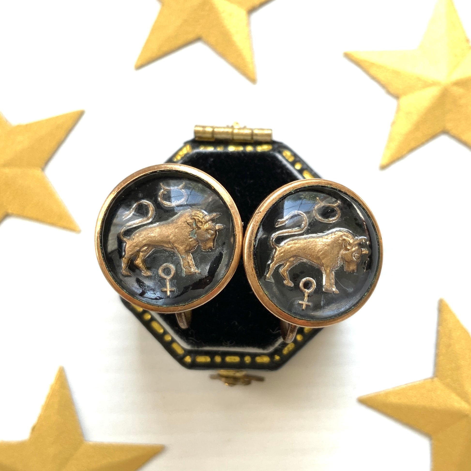 Screw-back earrings featuring an reverse carved design of a Taurus bull . 黒地にゴールドトーンで牡牛とそのシンボルが裏彫りされた、ヴィンテージのスクリューイヤリング。 