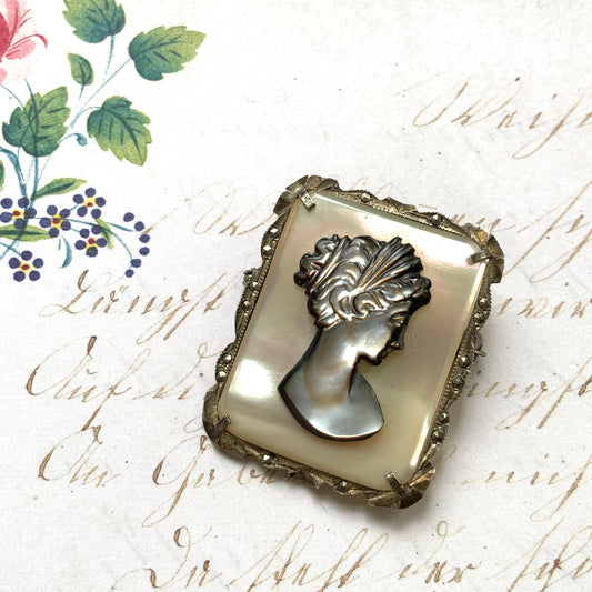 A brooch featuring a cameo of a lady’s profile carved in black mother of pearl, set against a white mother of pearl base. 白蝶貝をベースに、黒蝶貝で女性の横顔カメオをあしらったブローチ。 