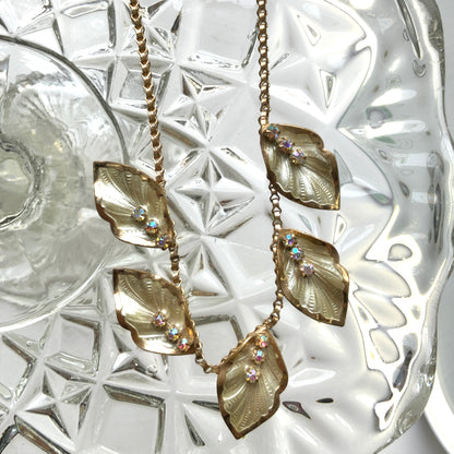 A graceful vintage necklace featuring leaf motifs in gold-tone metal with pearl white enamel detailing. エナメルリーフ×オーロラストーンのネックレス。