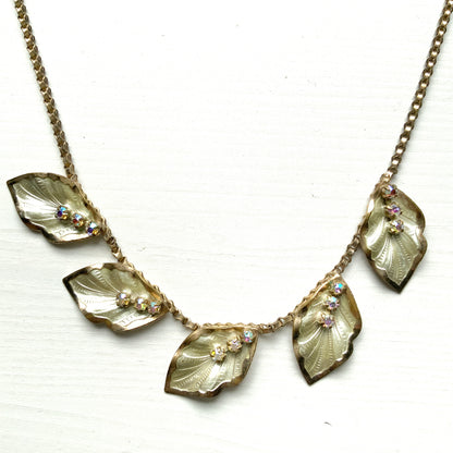 A graceful vintage necklace featuring leaf motifs in gold-tone metal with pearl white enamel detailing. エナメルリーフ×オーロラストーンのネックレス。