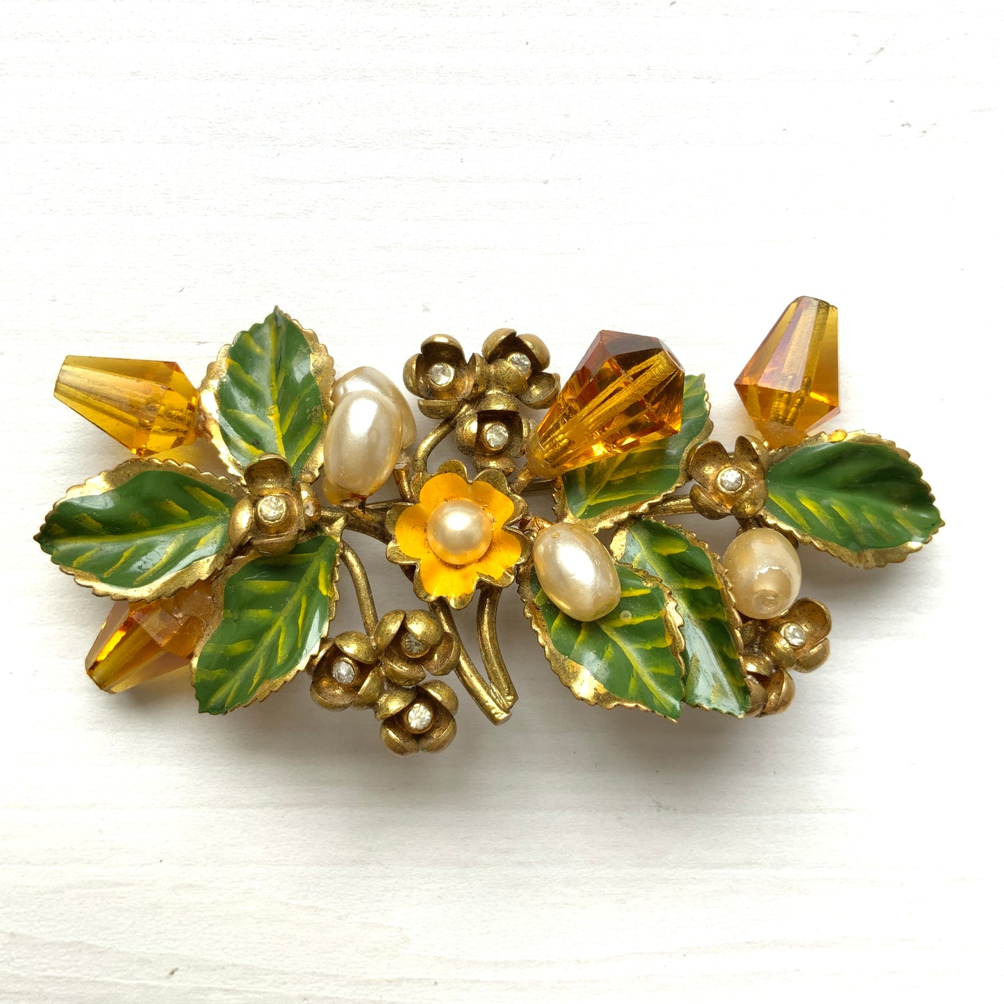A floral brooch adorned with green enamel leaves, amber glass beads, and faux pearls. グリーンのエナメルリーフに、アンバーグラスビーズやグラスパールをあしらったフラワーブローチ。