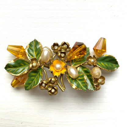 A floral brooch adorned with green enamel leaves, amber glass beads, and faux pearls. グリーンのエナメルリーフに、アンバーグラスビーズやグラスパールをあしらったフラワーブローチ。
