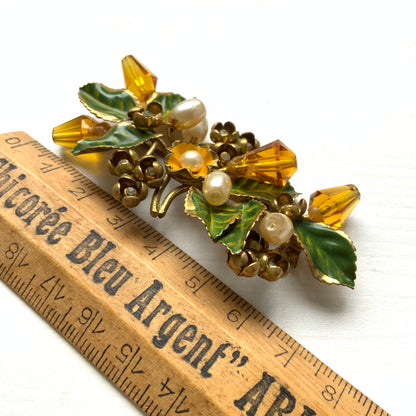 A floral brooch adorned with green enamel leaves, amber glass beads, and faux pearls. グリーンのエナメルリーフに、アンバーグラスビーズやグラスパールをあしらったフラワーブローチ。