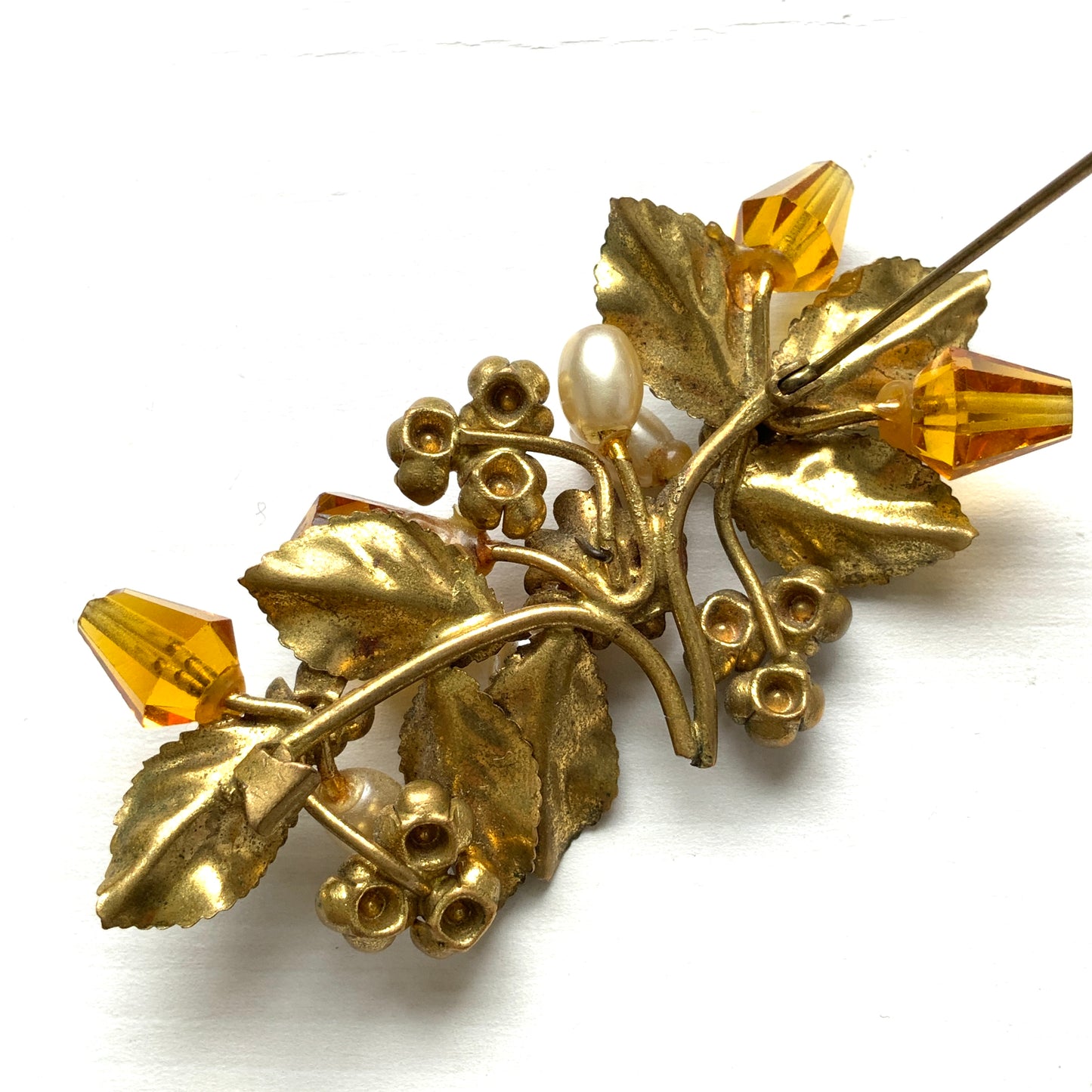 A floral brooch adorned with green enamel leaves, amber glass beads, and faux pearls. グリーンのエナメルリーフに、アンバーグラスビーズやグラスパールをあしらったフラワーブローチ。