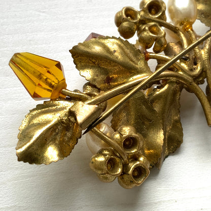 A floral brooch adorned with green enamel leaves, amber glass beads, and faux pearls. グリーンのエナメルリーフに、アンバーグラスビーズやグラスパールをあしらったフラワーブローチ。