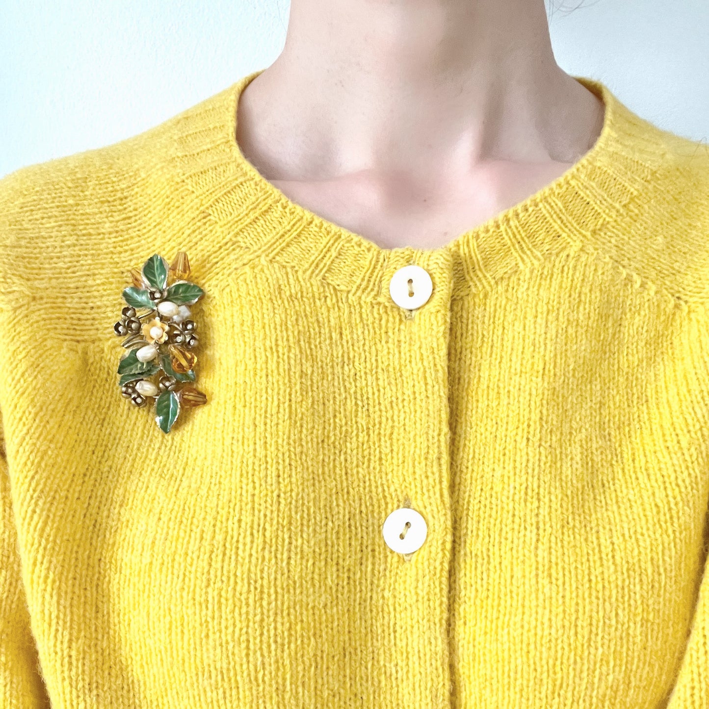 A floral brooch adorned with green enamel leaves, amber glass beads, and faux pearls. グリーンのエナメルリーフに、アンバーグラスビーズやグラスパールをあしらったフラワーブローチ。
