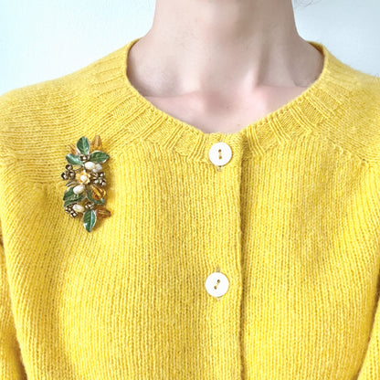 A floral brooch adorned with green enamel leaves, amber glass beads, and faux pearls. グリーンのエナメルリーフに、アンバーグラスビーズやグラスパールをあしらったフラワーブローチ。