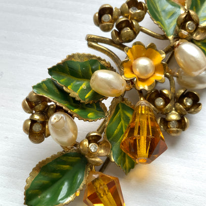 A floral brooch adorned with green enamel leaves, amber glass beads, and faux pearls. グリーンのエナメルリーフに、アンバーグラスビーズやグラスパールをあしらったフラワーブローチ。
