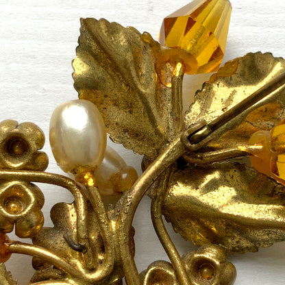 A floral brooch adorned with green enamel leaves, amber glass beads, and faux pearls. グリーンのエナメルリーフに、アンバーグラスビーズやグラスパールをあしらったフラワーブローチ。