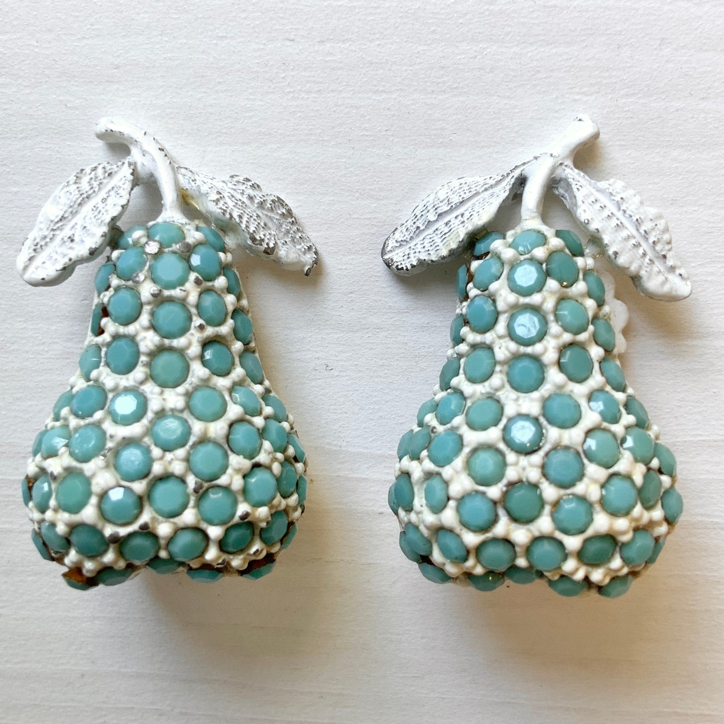 White pear-shaped clip earrings set with turquoise glass stones. ターコイズカラーのガラスストーンが散りばめられた、白い洋梨モチーフのクリップイヤリング。