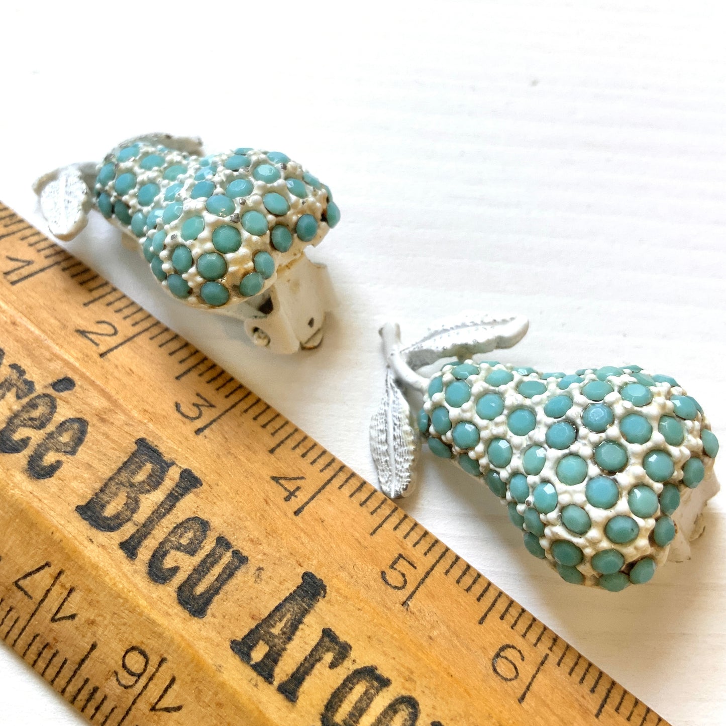 White pear-shaped clip earrings set with turquoise glass stones. ターコイズカラーのガラスストーンが散りばめられた、白い洋梨モチーフのクリップイヤリング。