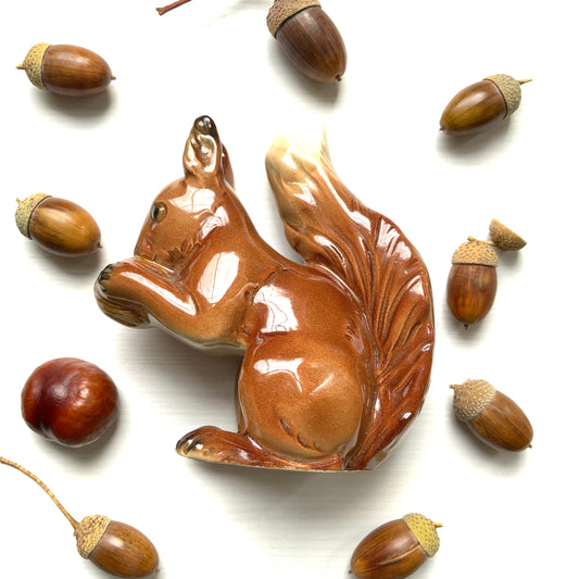 A charming ceramic squirrel figurine holding a nut. ナッツを抱えた、愛らしいセラミック製のリスのフィギュリン。