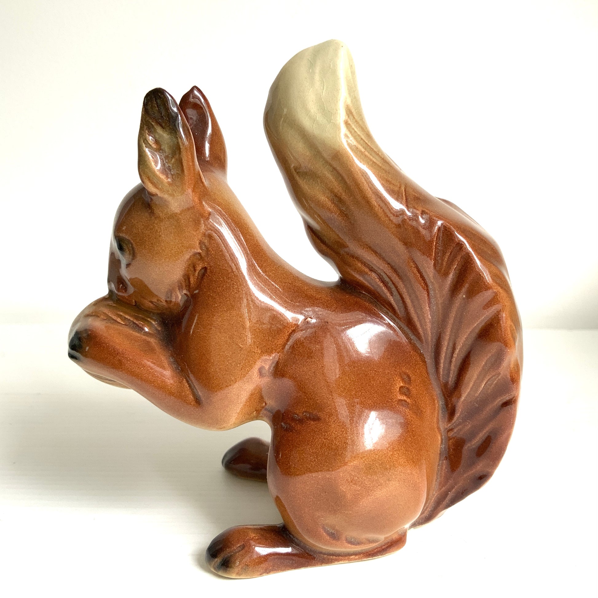 A charming ceramic squirrel figurine holding a nut. ナッツを抱えた、愛らしいセラミック製のリスのフィギュリン。