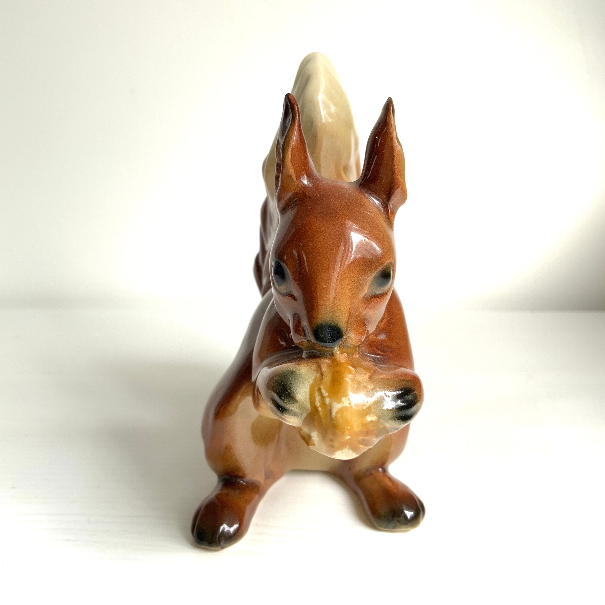 A charming ceramic squirrel figurine holding a nut. ナッツを抱えた、愛らしいセラミック製のリスのフィギュリン。