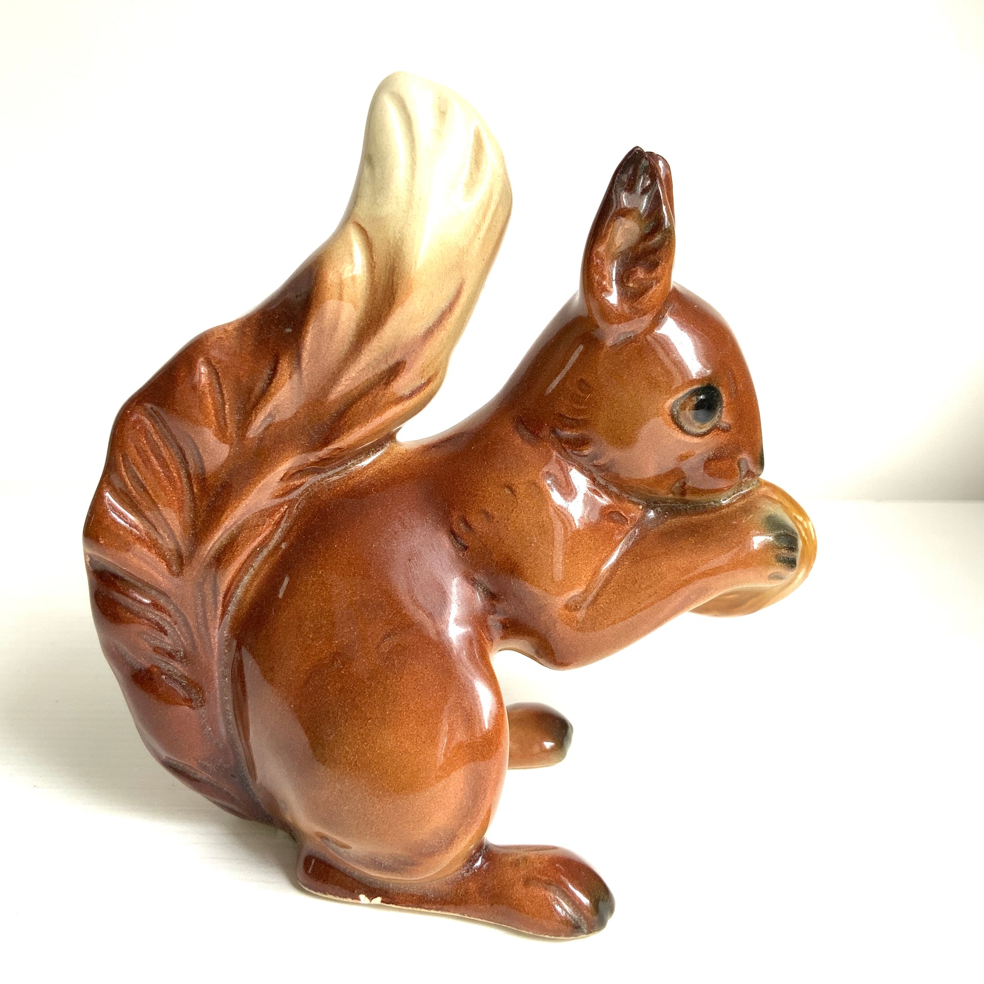 A charming ceramic squirrel figurine holding a nut. ナッツを抱えた、愛らしいセラミック製のリスのフィギュリン。