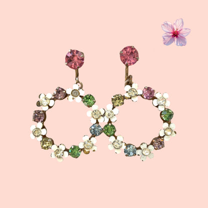 A pair of screw-back earrings featuring delicate white enamel flowers and a dangling hoop of rhinestones.  小さな白いエナメルの花とラインストーンのフープが揺れるスクリューイヤリング。 