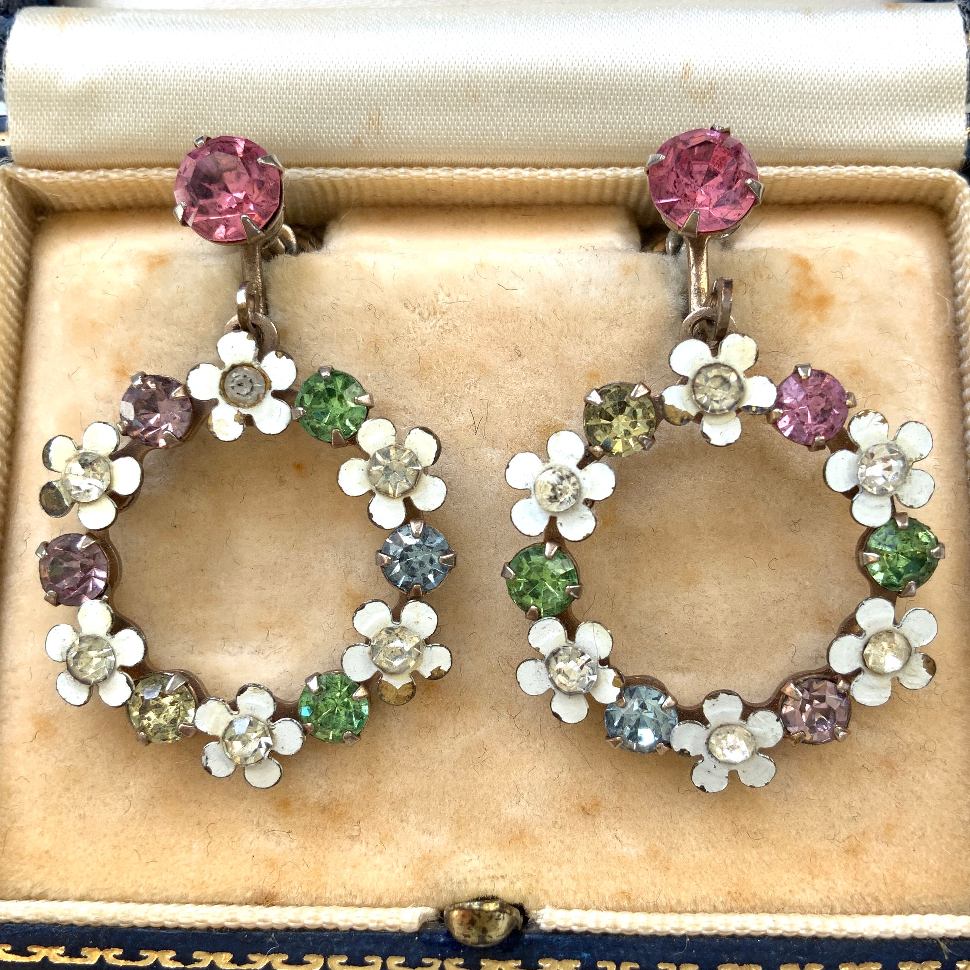 A pair of screw-back earrings featuring delicate white enamel flowers and a dangling hoop of rhinestones.  小さな白いエナメルの花とラインストーンのフープが揺れるスクリューイヤリング。 