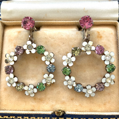 A pair of screw-back earrings featuring delicate white enamel flowers and a dangling hoop of rhinestones.  小さな白いエナメルの花とラインストーンのフープが揺れるスクリューイヤリング。 