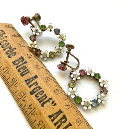 A pair of screw-back earrings featuring delicate white enamel flowers and a dangling hoop of rhinestones.  小さな白いエナメルの花とラインストーンのフープが揺れるスクリューイヤリング。 