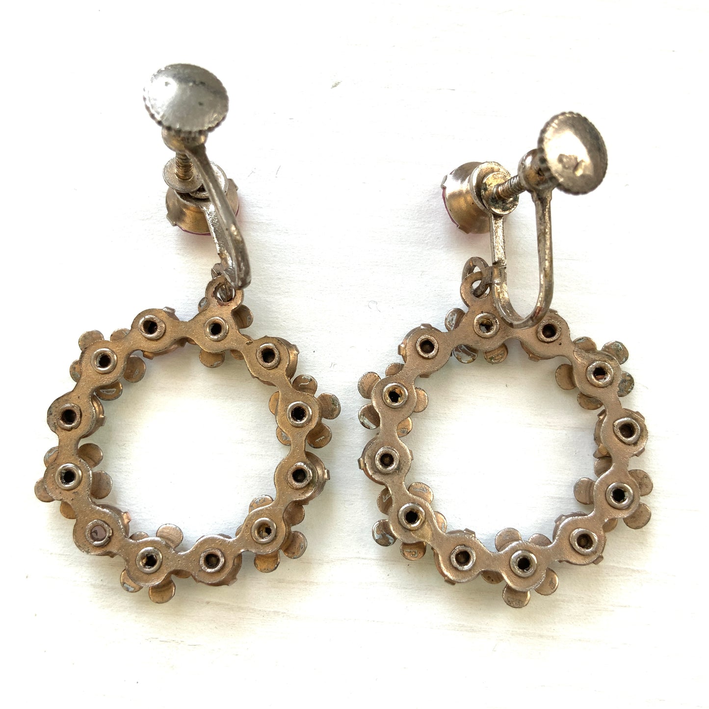 A pair of screw-back earrings featuring delicate white enamel flowers and a dangling hoop of rhinestones.  小さな白いエナメルの花とラインストーンのフープが揺れるスクリューイヤリング。 