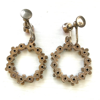 A pair of screw-back earrings featuring delicate white enamel flowers and a dangling hoop of rhinestones.  小さな白いエナメルの花とラインストーンのフープが揺れるスクリューイヤリング。 