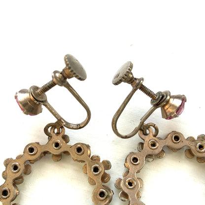 A pair of screw-back earrings featuring delicate white enamel flowers and a dangling hoop of rhinestones.  小さな白いエナメルの花とラインストーンのフープが揺れるスクリューイヤリング。 