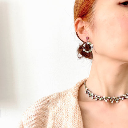 A pair of screw-back earrings featuring delicate white enamel flowers and a dangling hoop of rhinestones.  小さな白いエナメルの花とラインストーンのフープが揺れるスクリューイヤリング。 