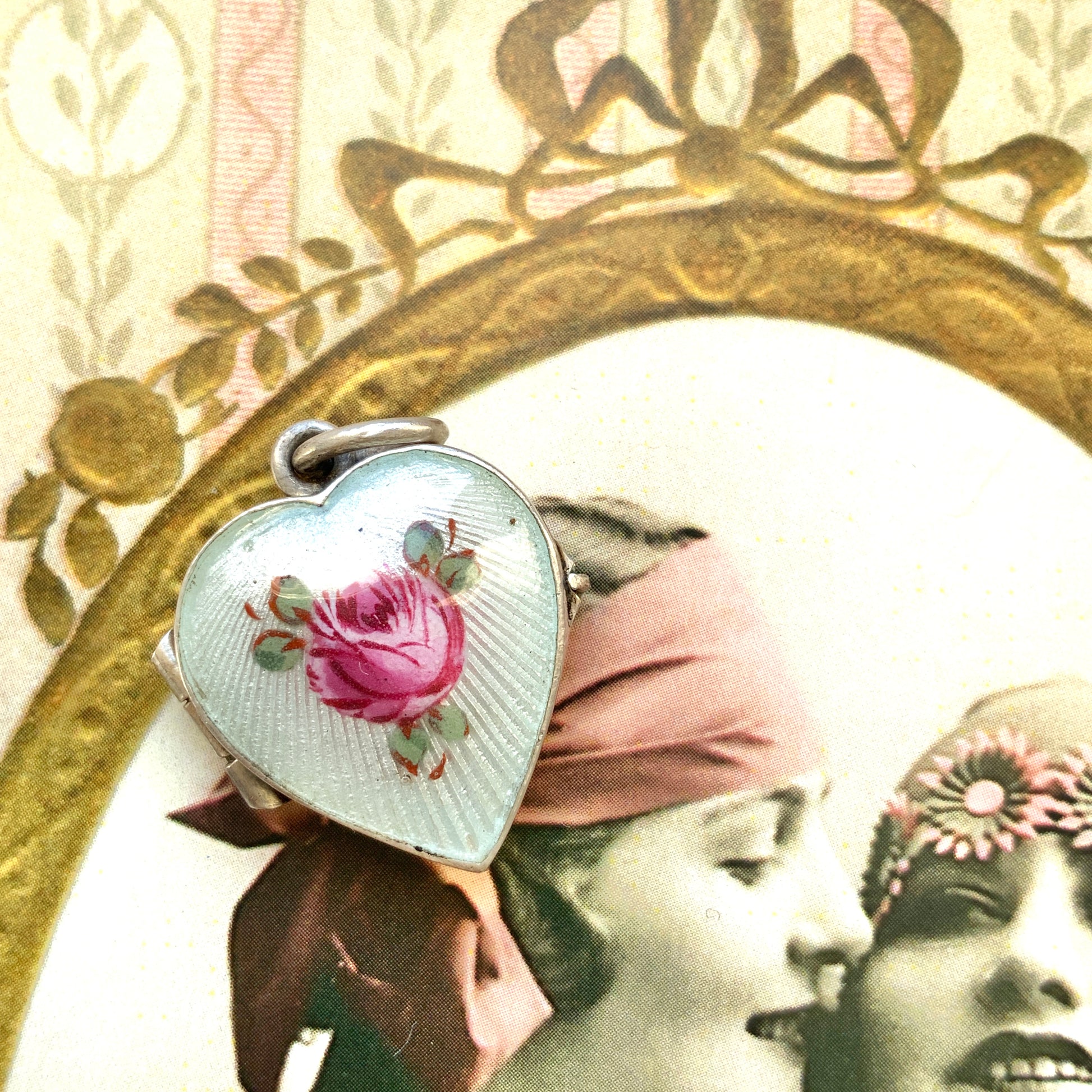 A silver heart locket featuring white guilloché enamel with a very subtle pale mint-green undertone, decorated with a rose motif.  ごく淡いミントグリーンのシェードを含んだホワイトギヨシェエナメルに、薔薇のモチーフが描かれたシルバーのハートロケット。