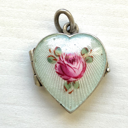 A silver heart locket featuring white guilloché enamel with a very subtle pale mint-green undertone, decorated with a rose motif.  ごく淡いミントグリーンのシェードを含んだホワイトギヨシェエナメルに、薔薇のモチーフが描かれたシルバーのハートロケット。