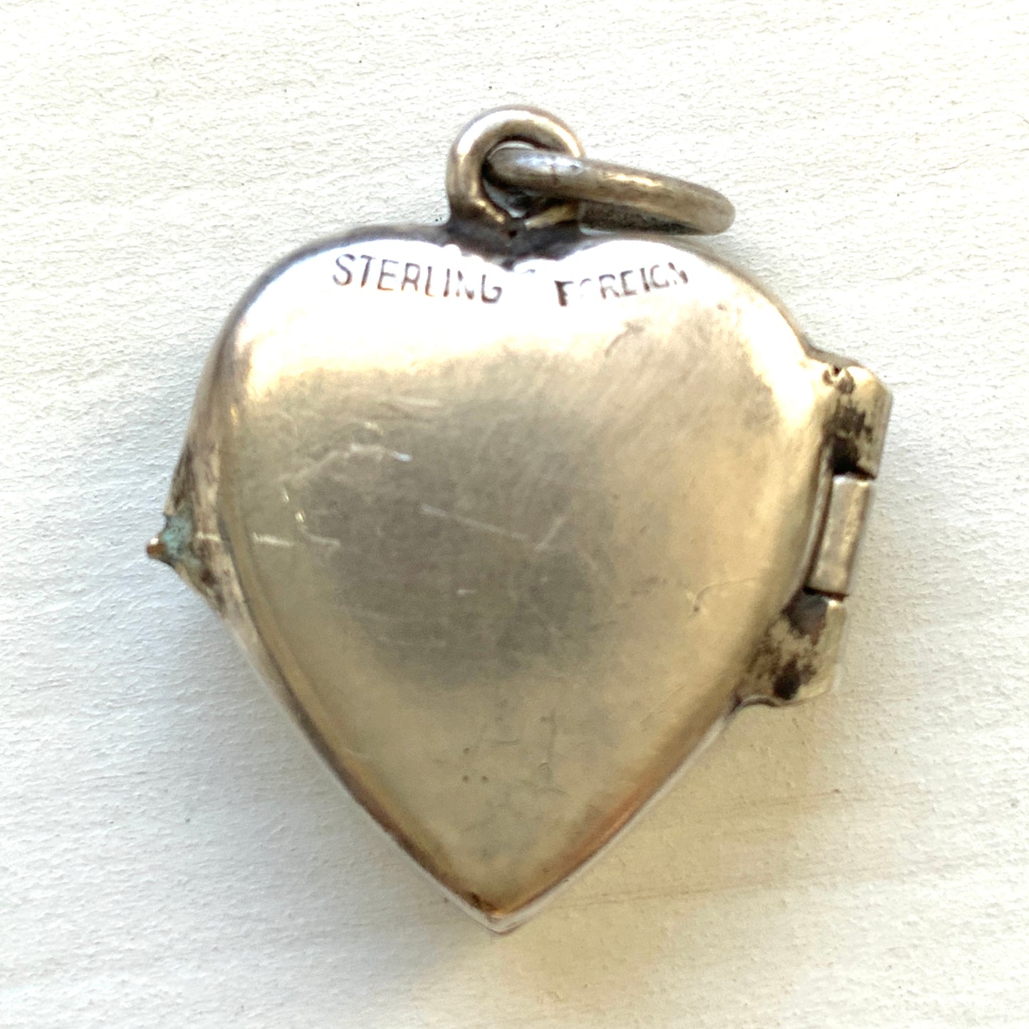 A silver heart locket featuring white guilloché enamel with a very subtle pale mint-green undertone, decorated with a rose motif.  ごく淡いミントグリーンのシェードを含んだホワイトギヨシェエナメルに、薔薇のモチーフが描かれたシルバーのハートロケット。