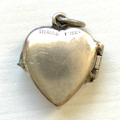 A silver heart locket featuring white guilloché enamel with a very subtle pale mint-green undertone, decorated with a rose motif.  ごく淡いミントグリーンのシェードを含んだホワイトギヨシェエナメルに、薔薇のモチーフが描かれたシルバーのハートロケット。