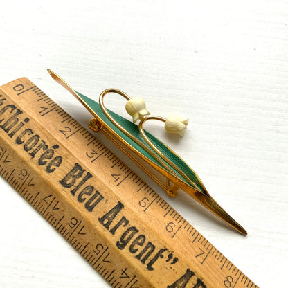 A brooch featuring lily of the valley set against a green enamel leaf. グリーンのエナメルリーフに、スズランをあしらったブローチ。