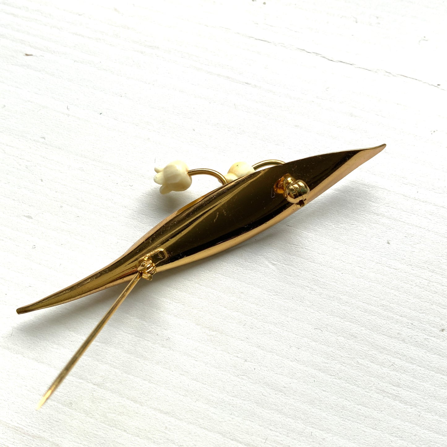 A brooch featuring lily of the valley set against a green enamel leaf. グリーンのエナメルリーフに、スズランをあしらったブローチ。