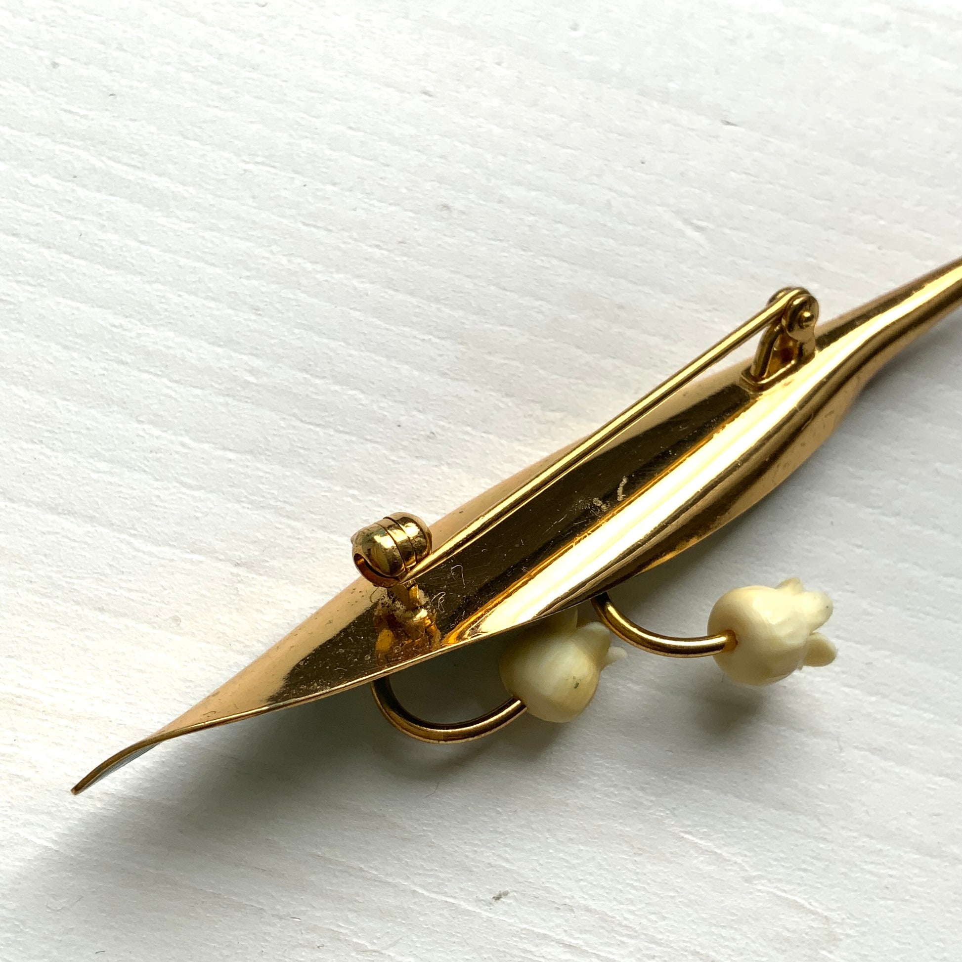A brooch featuring lily of the valley set against a green enamel leaf. グリーンのエナメルリーフに、スズランをあしらったブローチ。