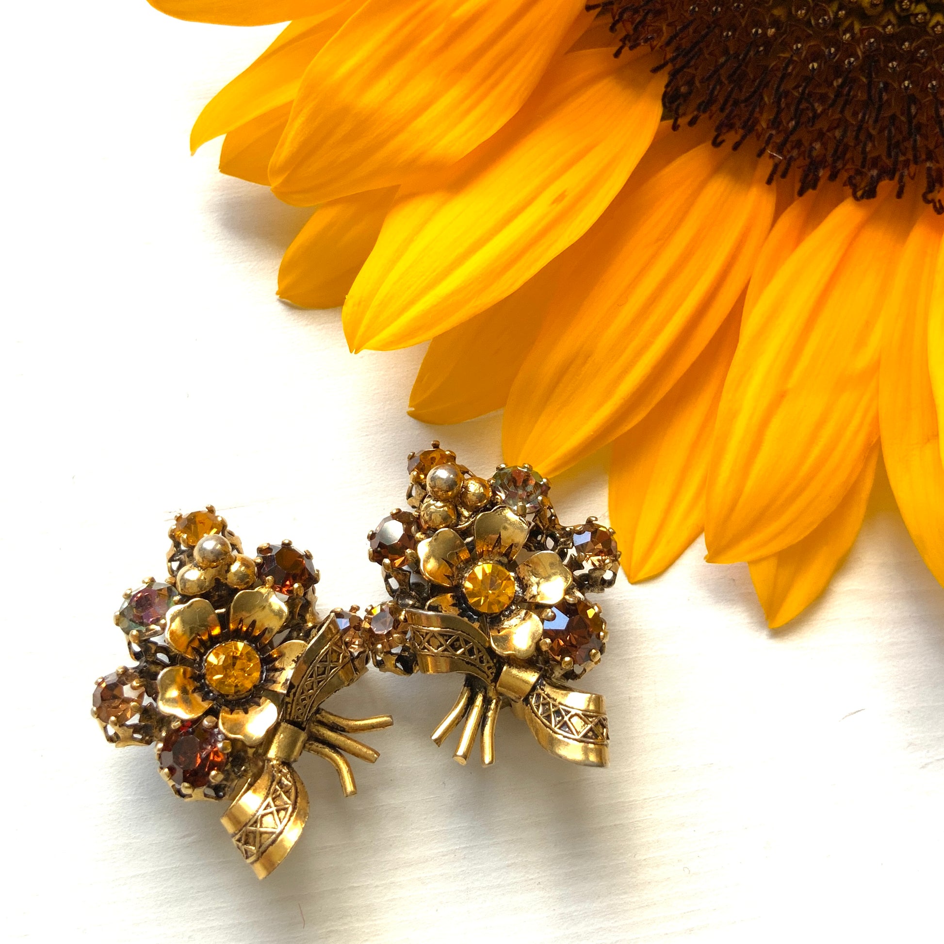 Clip-on earrings featuring a bouquet of gold-tone flowers adorned with amber, yellow, and orange rhinestones. ゴールドトーンのお花を、アンバー・イエロー・オレンジ系のラインストーンでブーケに仕立てたクリップイヤリング。 