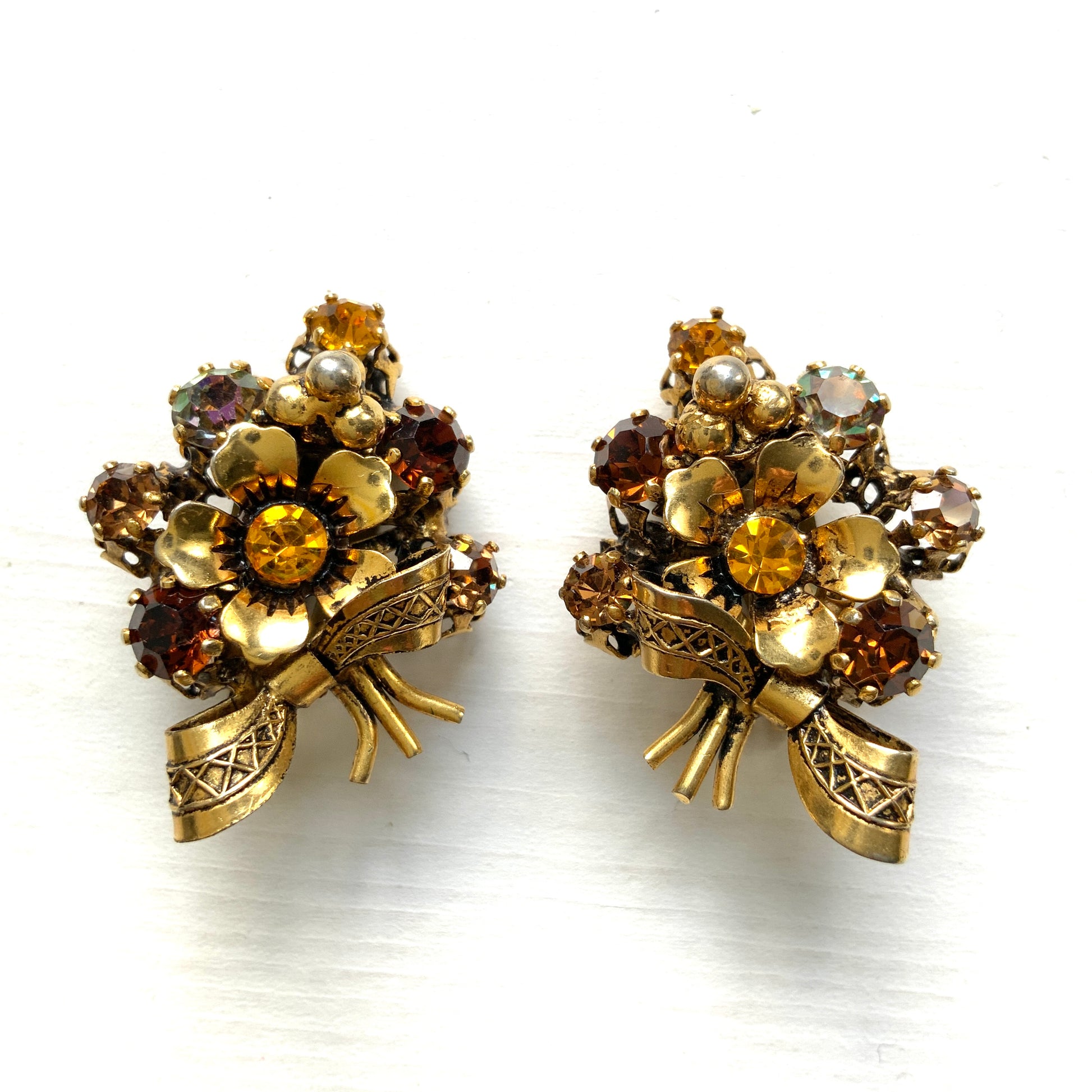 Clip-on earrings featuring a bouquet of gold-tone flowers adorned with amber, yellow, and orange rhinestones. ゴールドトーンのお花を、アンバー・イエロー・オレンジ系のラインストーンでブーケに仕立てたクリップイヤリング。 