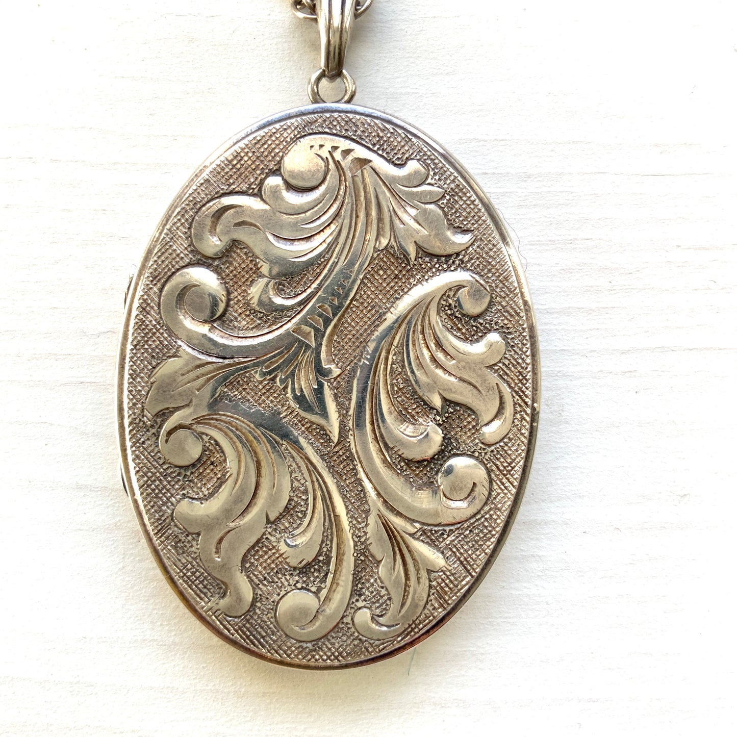 A silver locket necklace beautifully engraved with an elegant botanical motif.  美しい植物模様が彫られた、シルバーのロケットネックレス。