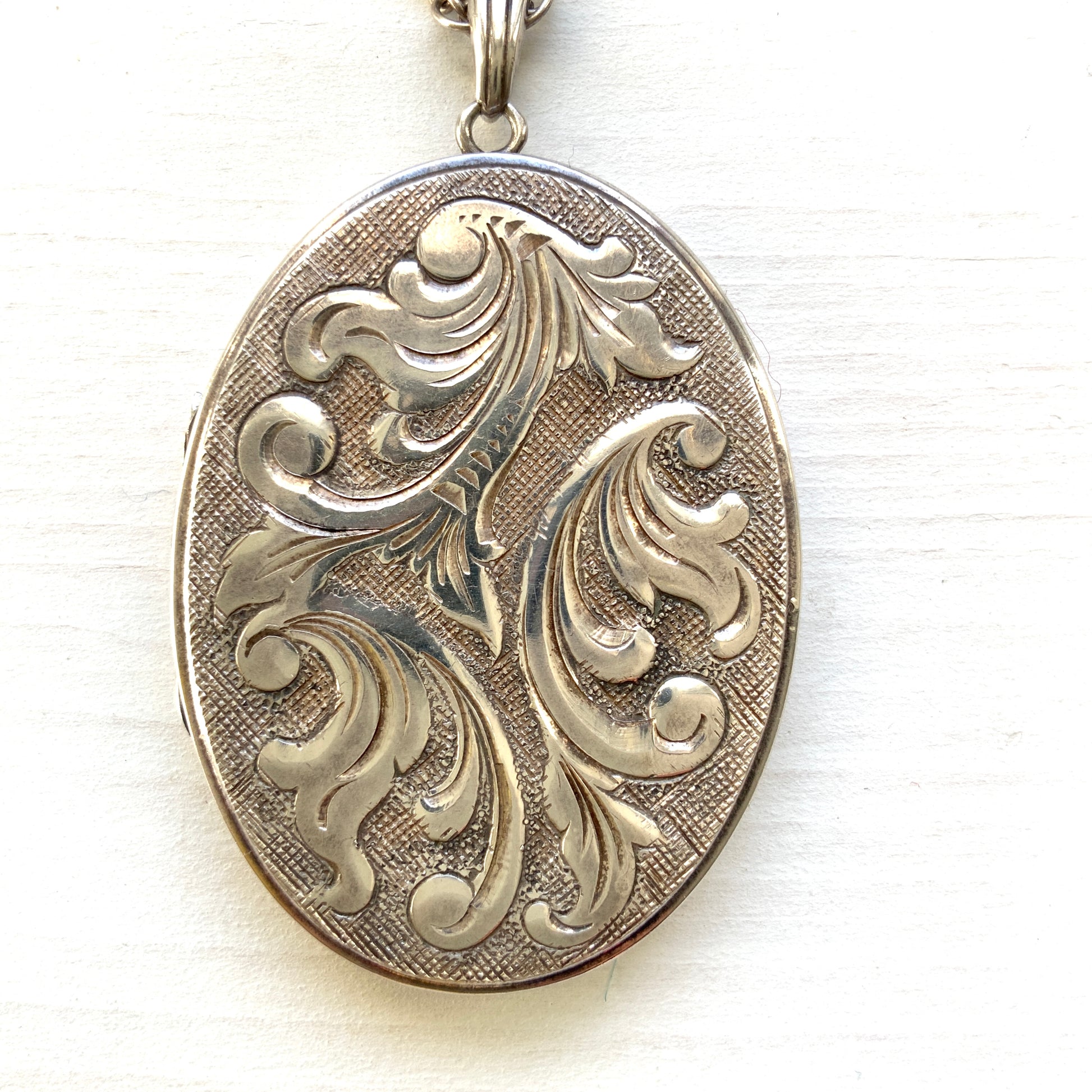 A silver locket necklace beautifully engraved with an elegant botanical motif.  美しい植物模様が彫られた、シルバーのロケットネックレス。