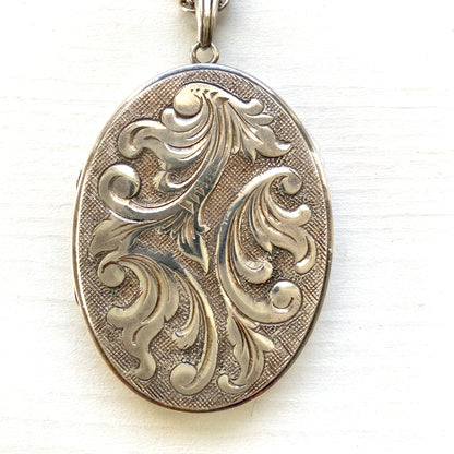 A silver locket necklace beautifully engraved with an elegant botanical motif.  美しい植物模様が彫られた、シルバーのロケットネックレス。