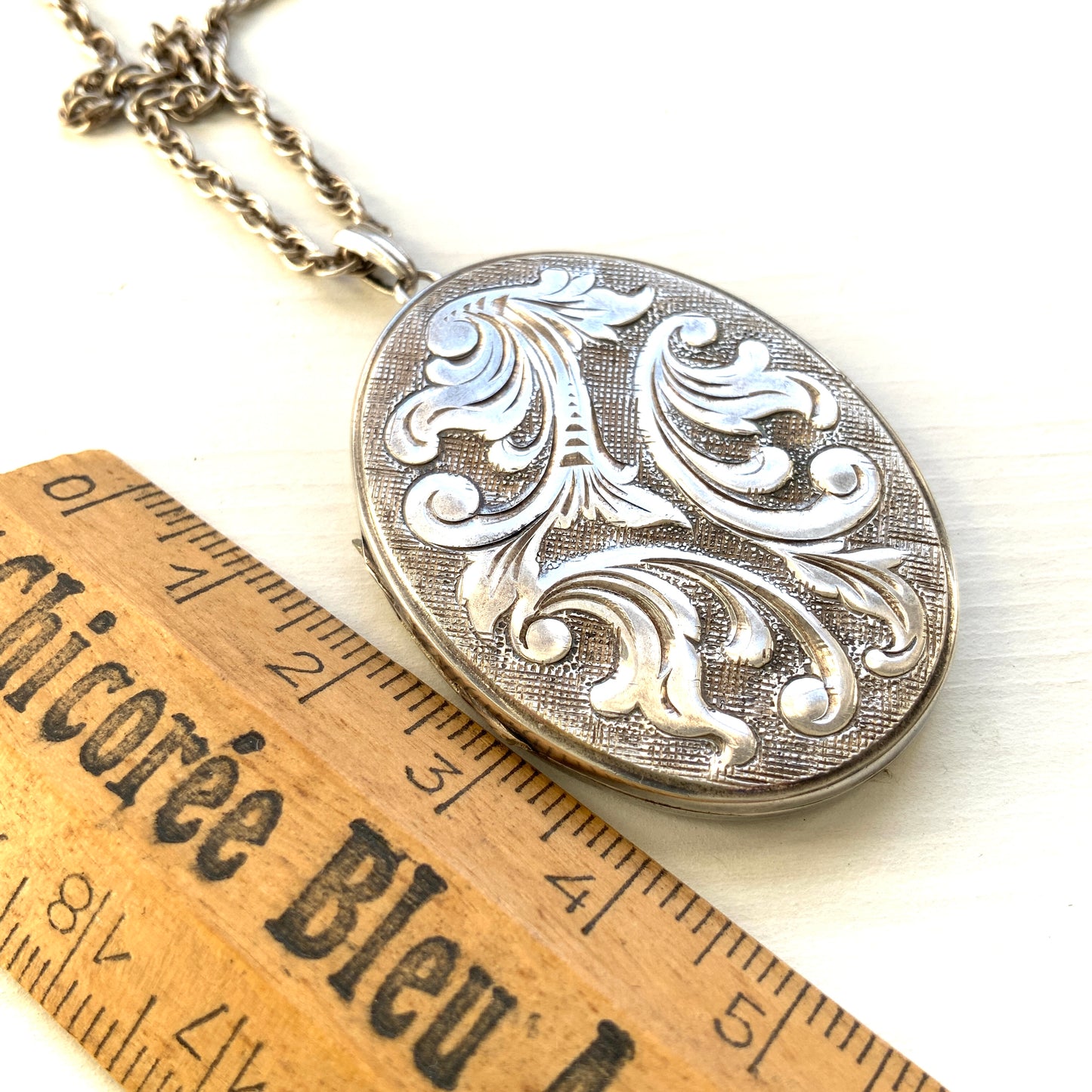 A silver locket necklace beautifully engraved with an elegant botanical motif.  美しい植物模様が彫られた、シルバーのロケットネックレス。