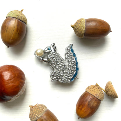 A silver-tone squirrel brooch holding a faux pearl acorn. シルバートーンのきらめくボディに、フェイクパールの実を抱えたリスのブローチ。