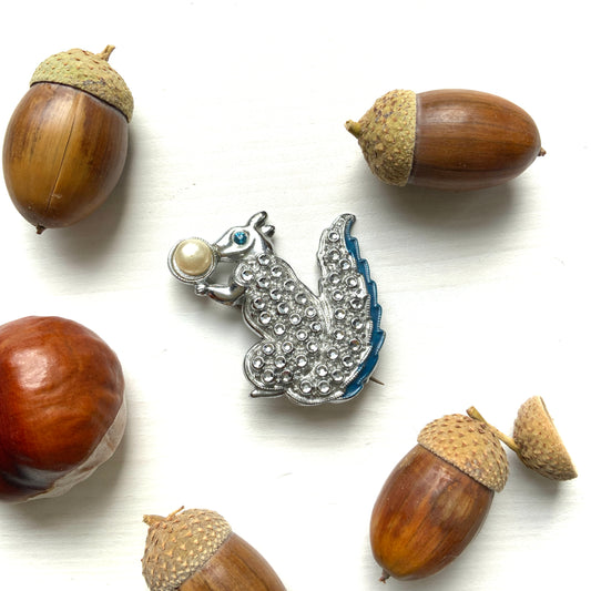 A silver-tone squirrel brooch holding a faux pearl acorn. シルバートーンのきらめくボディに、フェイクパールの実を抱えたリスのブローチ。