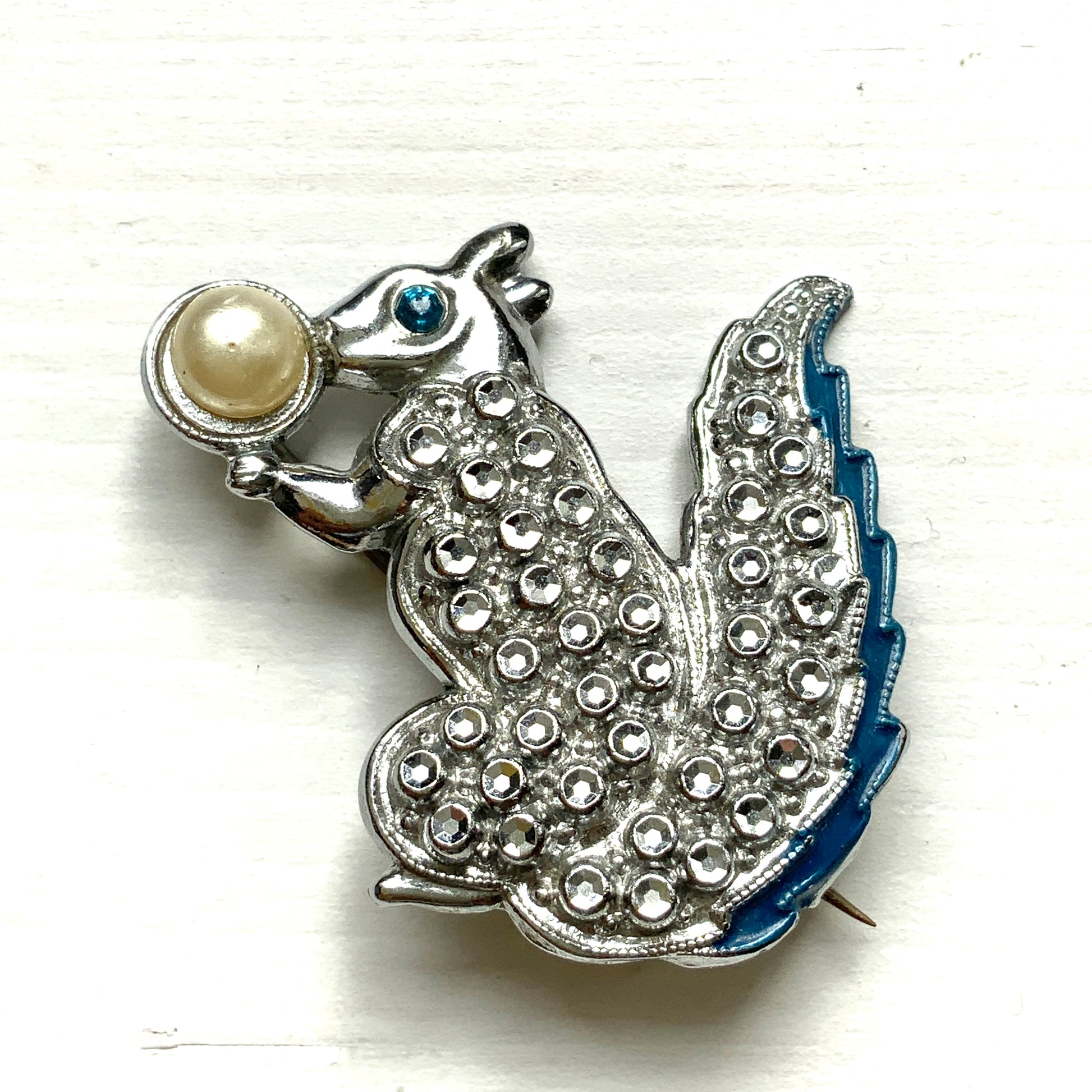 A silver-tone squirrel brooch holding a faux pearl acorn. シルバートーンのきらめくボディに、フェイクパールの実を抱えたリスのブローチ。