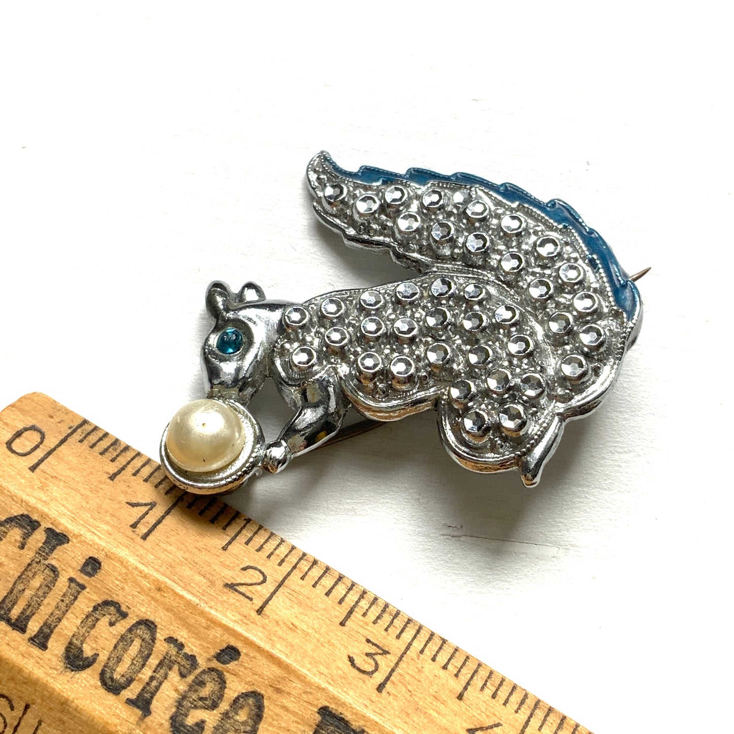 A silver-tone squirrel brooch holding a faux pearl acorn. シルバートーンのきらめくボディに、フェイクパールの実を抱えたリスのブローチ。