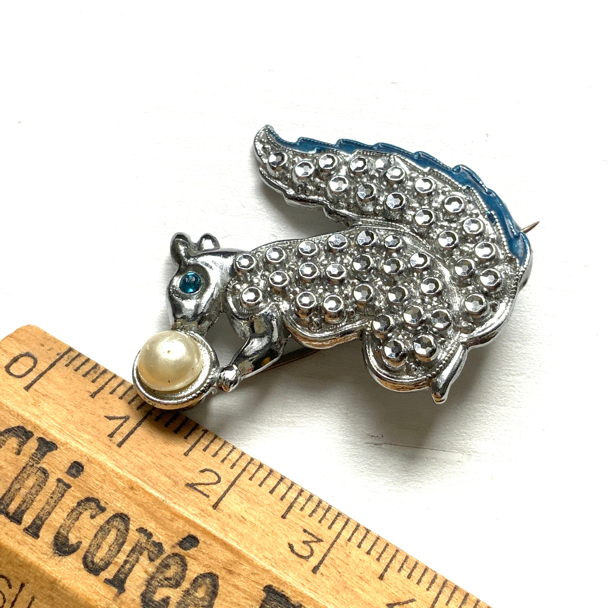 A silver-tone squirrel brooch holding a faux pearl acorn. シルバートーンのきらめくボディに、フェイクパールの実を抱えたリスのブローチ。